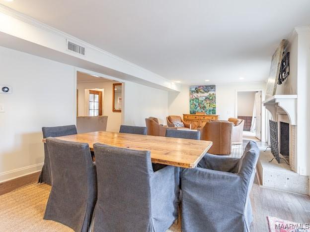 dining room featuring a fireplace with raised hearth, visible vents, baseboards, and wood finished floors