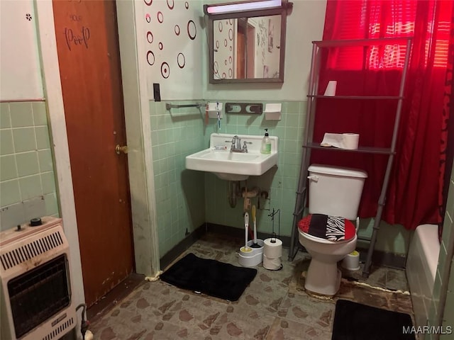 bathroom with heating unit, tile walls, a wainscoted wall, toilet, and a sink
