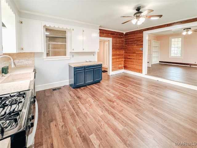 kitchen featuring wood walls, crown molding, blue cabinetry, black gas stove, and white cabinetry