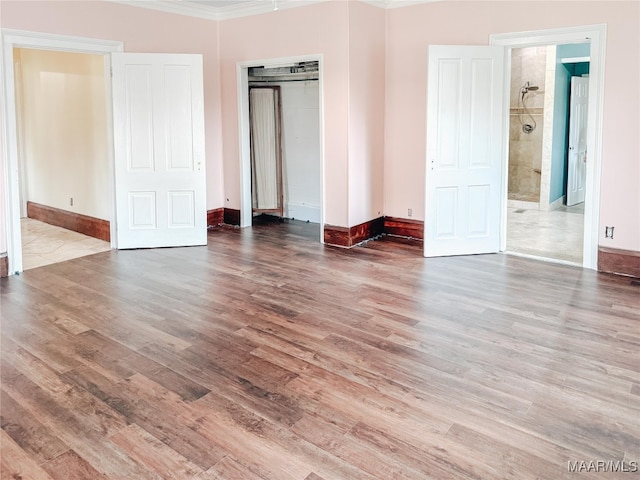 unfurnished bedroom featuring ornamental molding, a closet, connected bathroom, and hardwood / wood-style floors