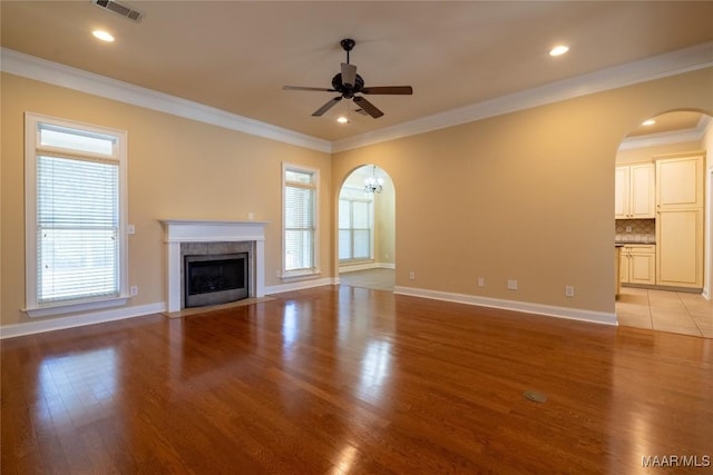 unfurnished living room featuring a tiled fireplace, ceiling fan, a healthy amount of sunlight, and ornamental molding