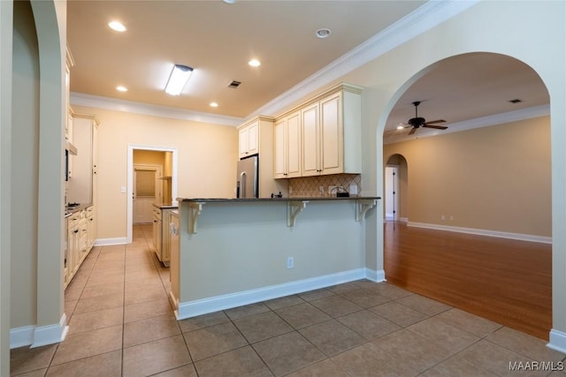 kitchen featuring a breakfast bar, ceiling fan, stainless steel fridge, light tile patterned flooring, and kitchen peninsula