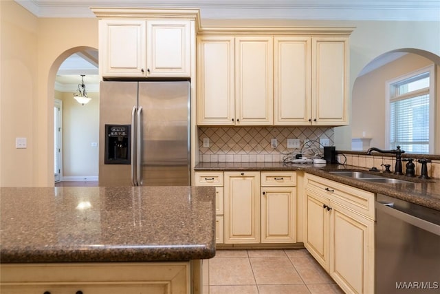 kitchen featuring backsplash, stainless steel appliances, sink, dark stone countertops, and cream cabinetry