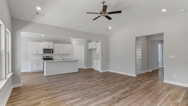 kitchen with a kitchen island with sink, light hardwood / wood-style flooring, white cabinets, range, and lofted ceiling