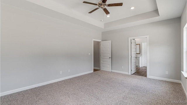 unfurnished bedroom with dark carpet, a raised ceiling, ensuite bath, and ceiling fan