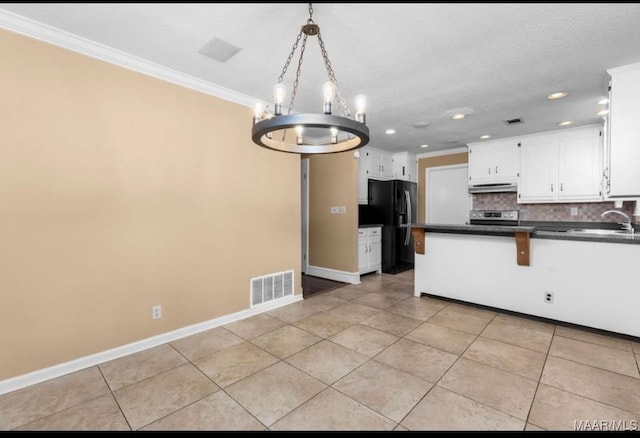 3033 Willow Lane Dr, Montgomery, AL 36109 - kitchen featuring under cabinet range hood, freestanding refrigerator, dark countertops, stainless steel range with electric stovetop, and crown molding