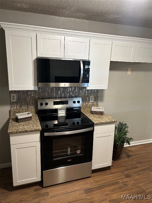 kitchen with appliances with stainless steel finishes, dark stone countertops, white cabinets, backsplash, and dark hardwood / wood-style flooring