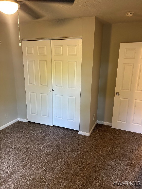 unfurnished bedroom featuring dark carpet, a closet, and ceiling fan