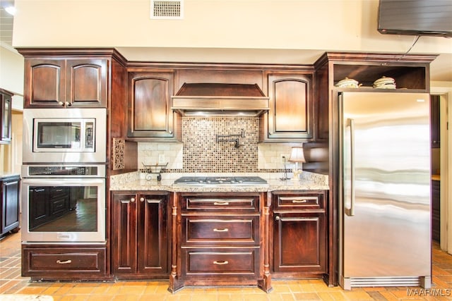 kitchen featuring decorative backsplash, light stone countertops, custom exhaust hood, and stainless steel appliances