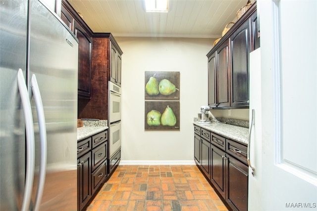 kitchen featuring stainless steel fridge, white double oven, dark brown cabinetry, and light stone counters