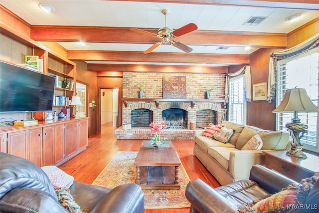 living room with a fireplace, light wood-type flooring, beam ceiling, ceiling fan, and wooden walls