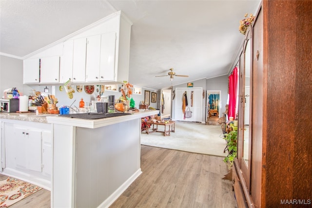 kitchen with white cabinets, lofted ceiling, kitchen peninsula, light hardwood / wood-style flooring, and crown molding