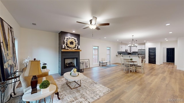 living room with ceiling fan with notable chandelier, a large fireplace, and light hardwood / wood-style floors