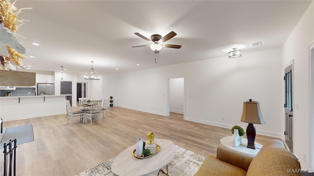 living room with ceiling fan with notable chandelier and light wood-type flooring