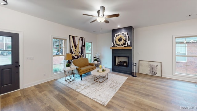 living area with ceiling fan, light wood-type flooring, and a large fireplace