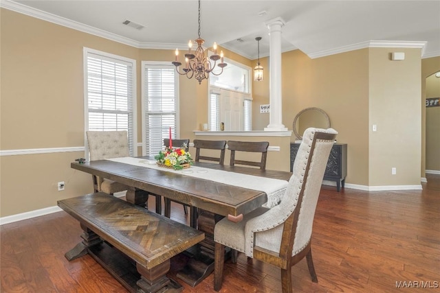 dining room featuring dark wood-type flooring, crown molding, an inviting chandelier, and ornate columns