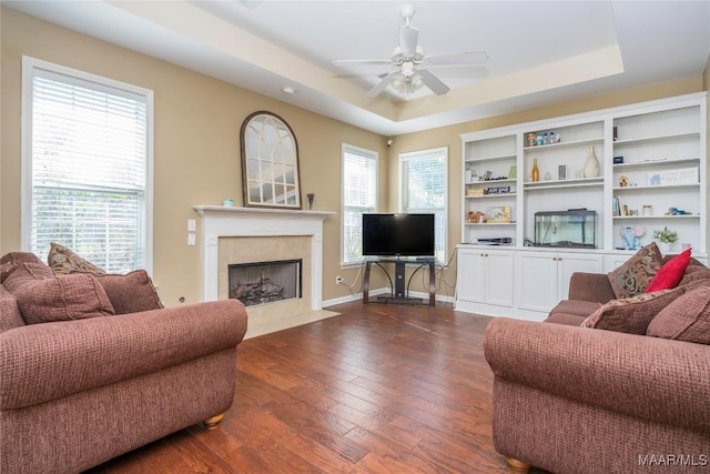 living room featuring a raised ceiling, a tiled fireplace, dark hardwood / wood-style floors, and ceiling fan