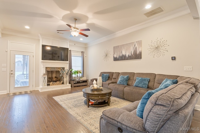 living room with crown molding, a stone fireplace, hardwood / wood-style floors, and ceiling fan