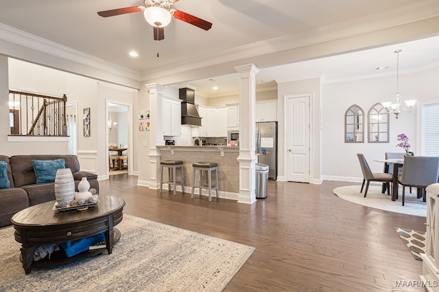 living room featuring ornate columns, ceiling fan with notable chandelier, crown molding, and dark hardwood / wood-style flooring