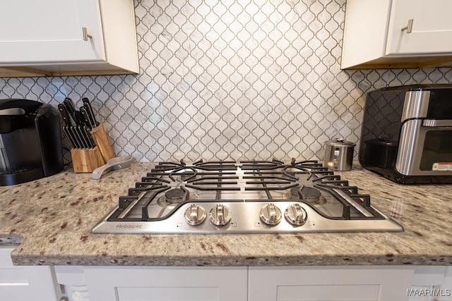 kitchen with stainless steel gas stovetop, tasteful backsplash, light stone counters, and white cabinets