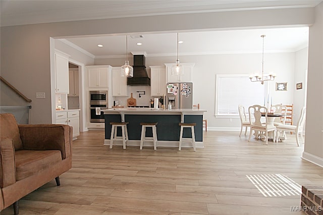 kitchen featuring hanging light fixtures, a kitchen island with sink, stainless steel appliances, custom range hood, and light hardwood / wood-style floors