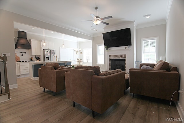 living room with crown molding, ceiling fan with notable chandelier, dark hardwood / wood-style floors, and a brick fireplace