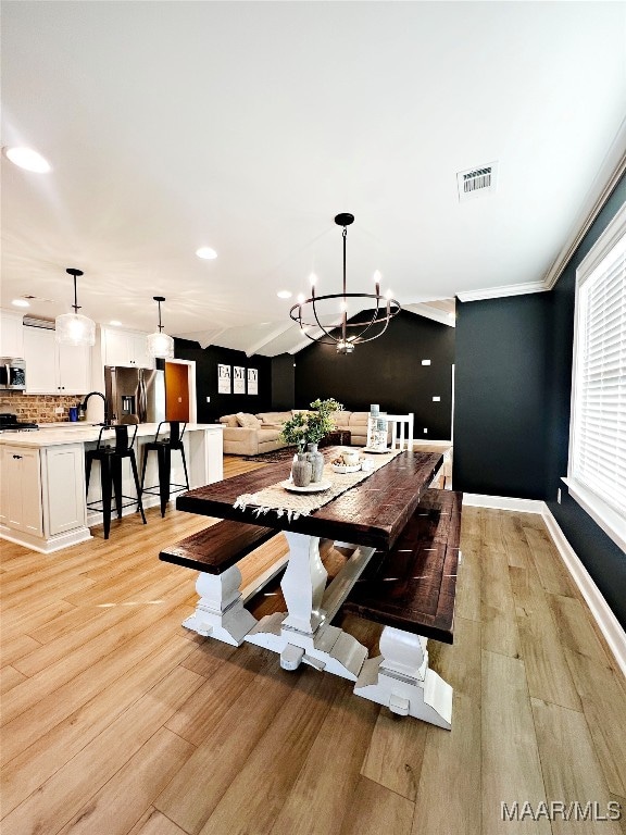 dining space featuring lofted ceiling, ornamental molding, an inviting chandelier, and light hardwood / wood-style flooring