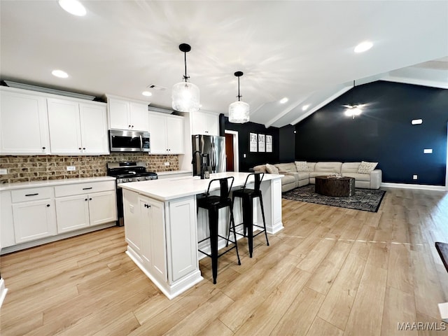 kitchen featuring an island with sink, white cabinets, vaulted ceiling, hanging light fixtures, and stainless steel appliances