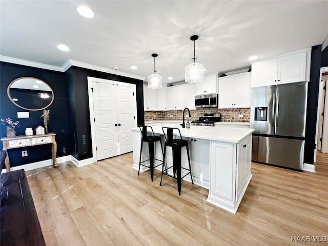 kitchen with appliances with stainless steel finishes, hanging light fixtures, light hardwood / wood-style floors, white cabinetry, and a kitchen island with sink