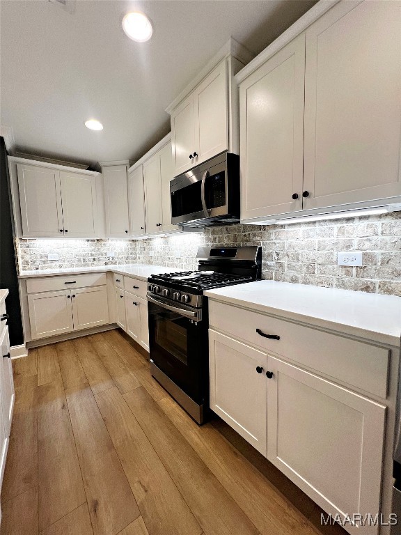 kitchen with stainless steel appliances, light wood-type flooring, tasteful backsplash, and white cabinetry