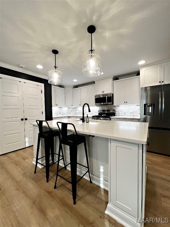 kitchen with decorative light fixtures, white cabinetry, stainless steel appliances, a spacious island, and light hardwood / wood-style floors