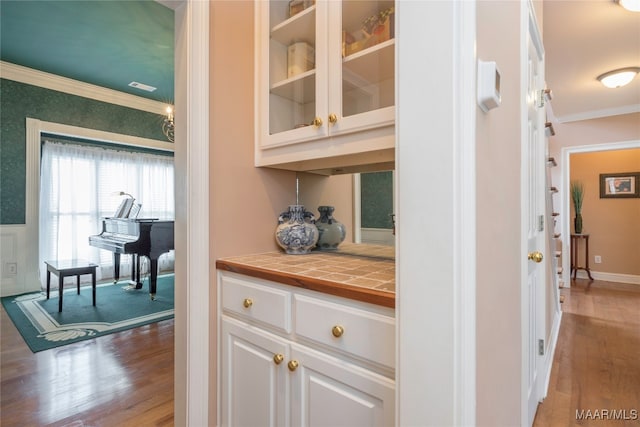 bar featuring white cabinets, hardwood / wood-style floors, tile countertops, and crown molding