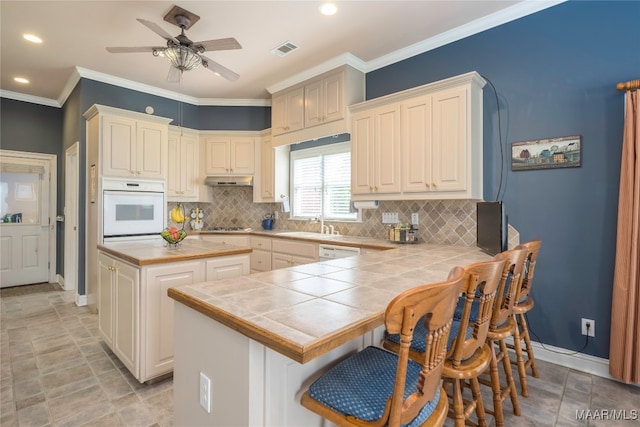 kitchen featuring crown molding, tile counters, white appliances, and sink