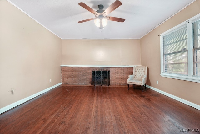 unfurnished room with dark hardwood / wood-style floors, a brick fireplace, crown molding, ceiling fan, and brick wall