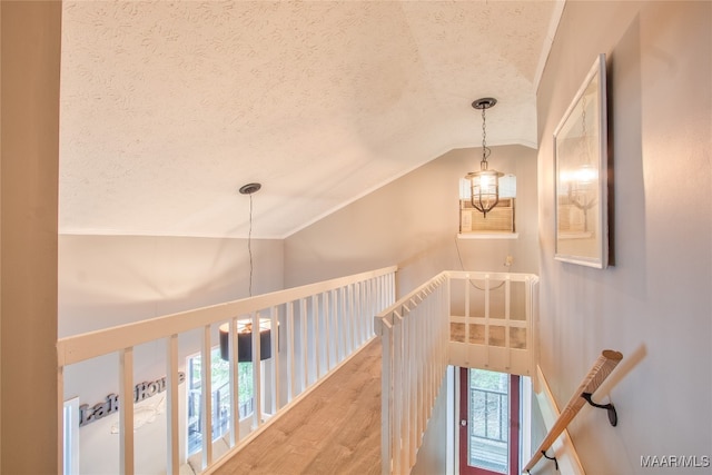 corridor featuring a textured ceiling, hardwood / wood-style floors, vaulted ceiling, and a chandelier