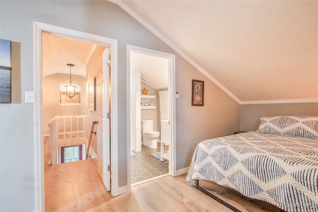 bedroom featuring light hardwood / wood-style floors, vaulted ceiling, crown molding, an inviting chandelier, and ensuite bathroom