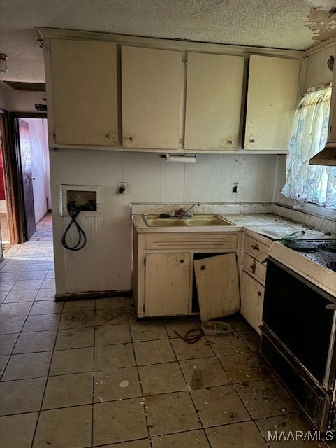 kitchen with a textured ceiling, cream cabinets, black electric range, and sink