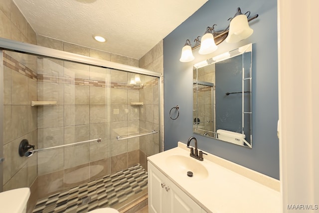 bathroom with a textured ceiling, a shower with door, vanity, and toilet