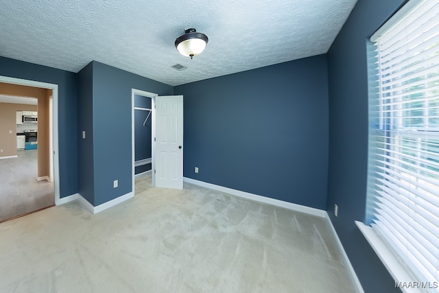 unfurnished bedroom featuring a textured ceiling, light colored carpet, and a closet