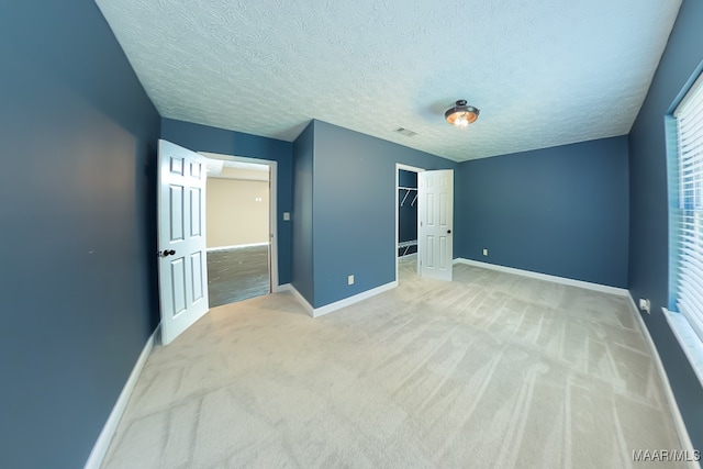 unfurnished bedroom with light colored carpet, a textured ceiling, a closet, and a spacious closet