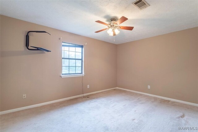 carpeted spare room featuring baseboards, ceiling fan, a textured ceiling, and visible vents