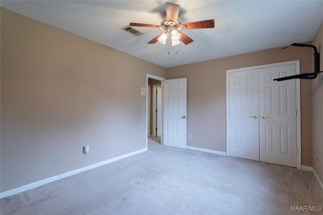 unfurnished bedroom with a textured ceiling, ceiling fan, light colored carpet, and a closet