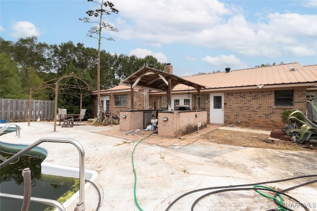rear view of house with a chimney, a patio area, brick siding, fence, and an outdoor kitchen