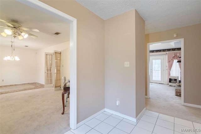 corridor with visible vents, light tile patterned floors, baseboards, a notable chandelier, and light carpet
