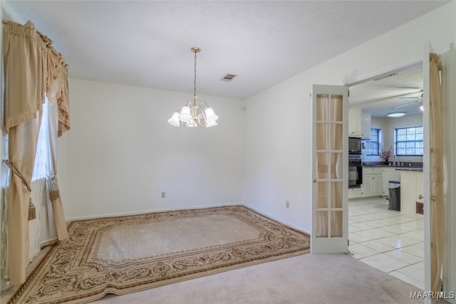 spare room with ceiling fan with notable chandelier, a textured ceiling, and light colored carpet