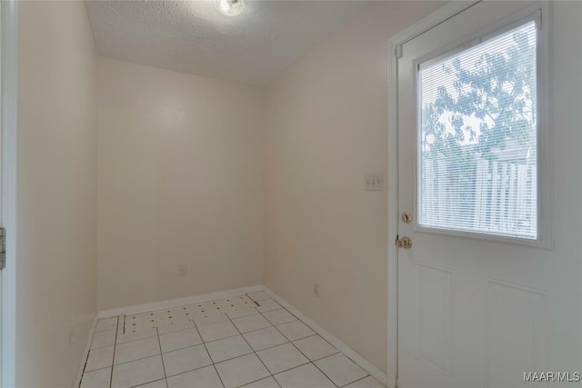 spare room featuring a healthy amount of sunlight, baseboards, light tile patterned floors, and a textured ceiling