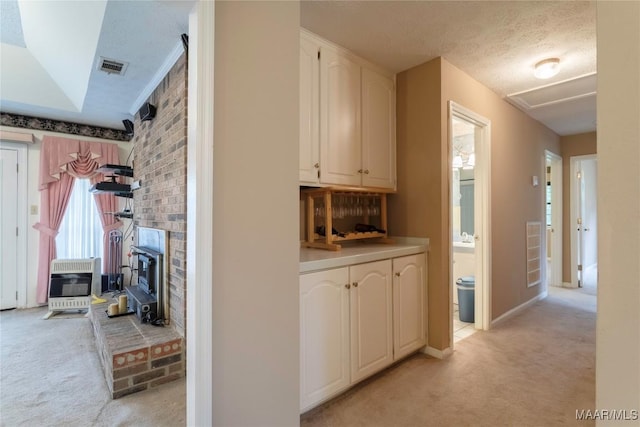 hallway featuring a textured ceiling, visible vents, light colored carpet, baseboards, and heating unit