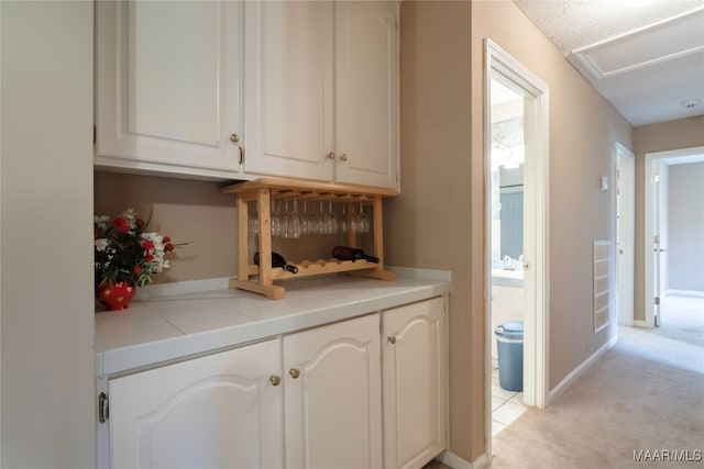 interior space with a textured ceiling, tile counters, light colored carpet, and white cabinets