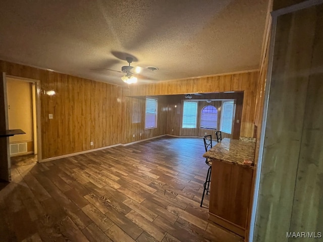 empty room featuring ceiling fan, a textured ceiling, wooden walls, and dark wood-type flooring