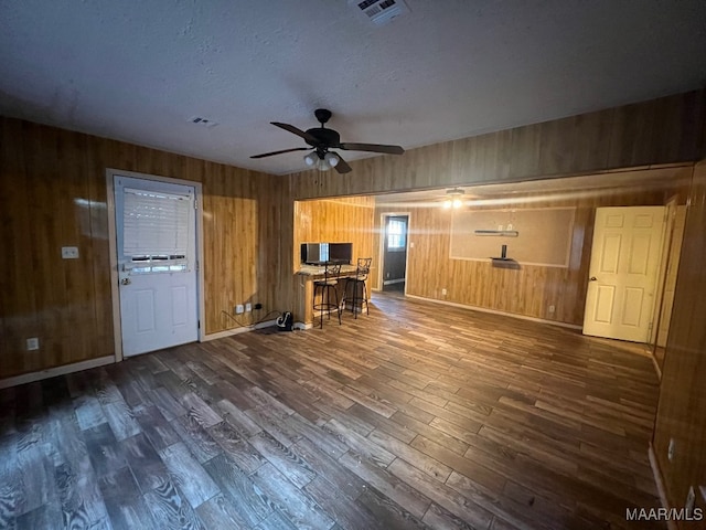 unfurnished living room featuring wooden walls, ceiling fan, a textured ceiling, and dark hardwood / wood-style flooring